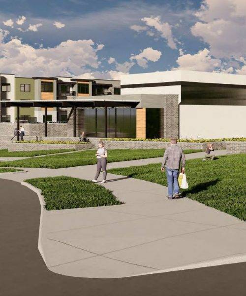 Three young adults interacting in front of an apartment building. One person, standing, gestures broadly with their arms while the other two sit on a wooden bench. The person on the left is in a white shirt, and the one on the right wears an orange shirt.
